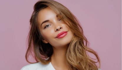 portrait of satisfied relaxed young female model tilts head has makeup fair hair dressed in white clothes poses against purple background has wel